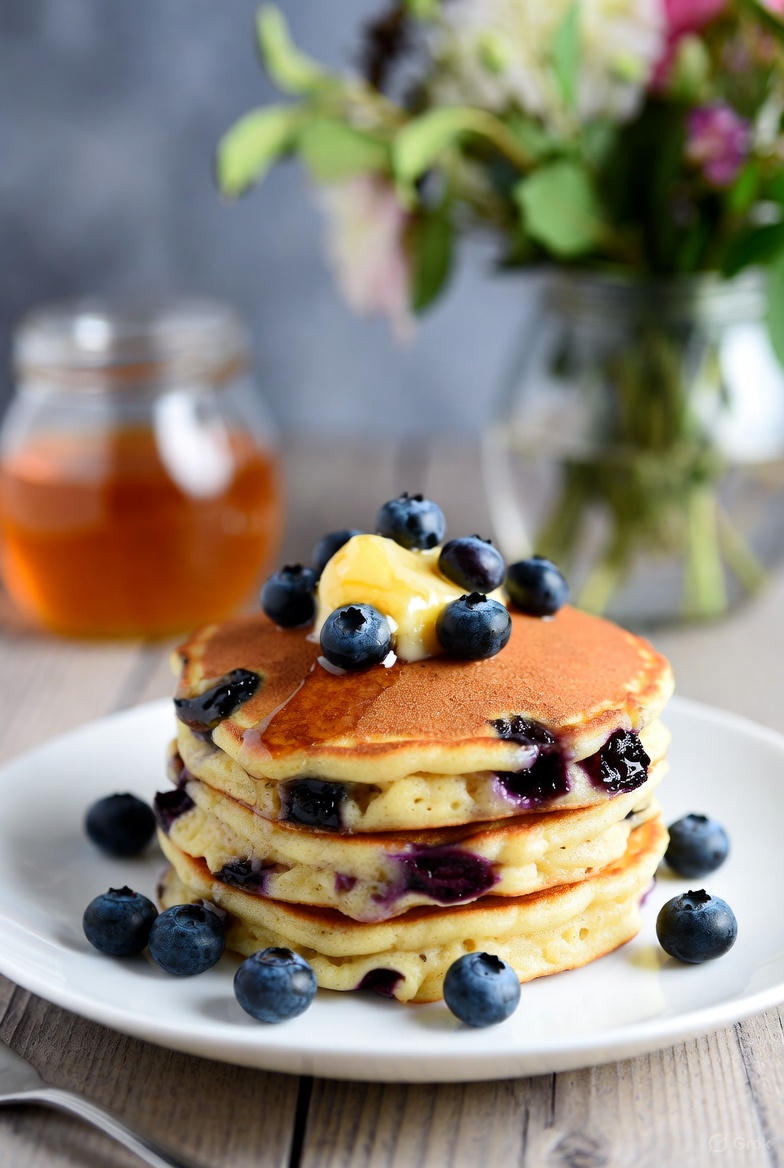 A stack of blueberry lemon ricotta pancakes topped with honey butter, ready to be enjoyed at home.
